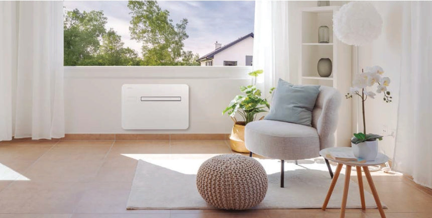Panasonic RAC Solo unit under window in neutral decor room. featuring wooden floor, white, padded chair, pale blue cushion, white bookcase and white rug. 